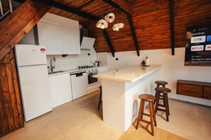 A modern kitchen with white cabinetry, a central island with stools, and a wooden ceiling.