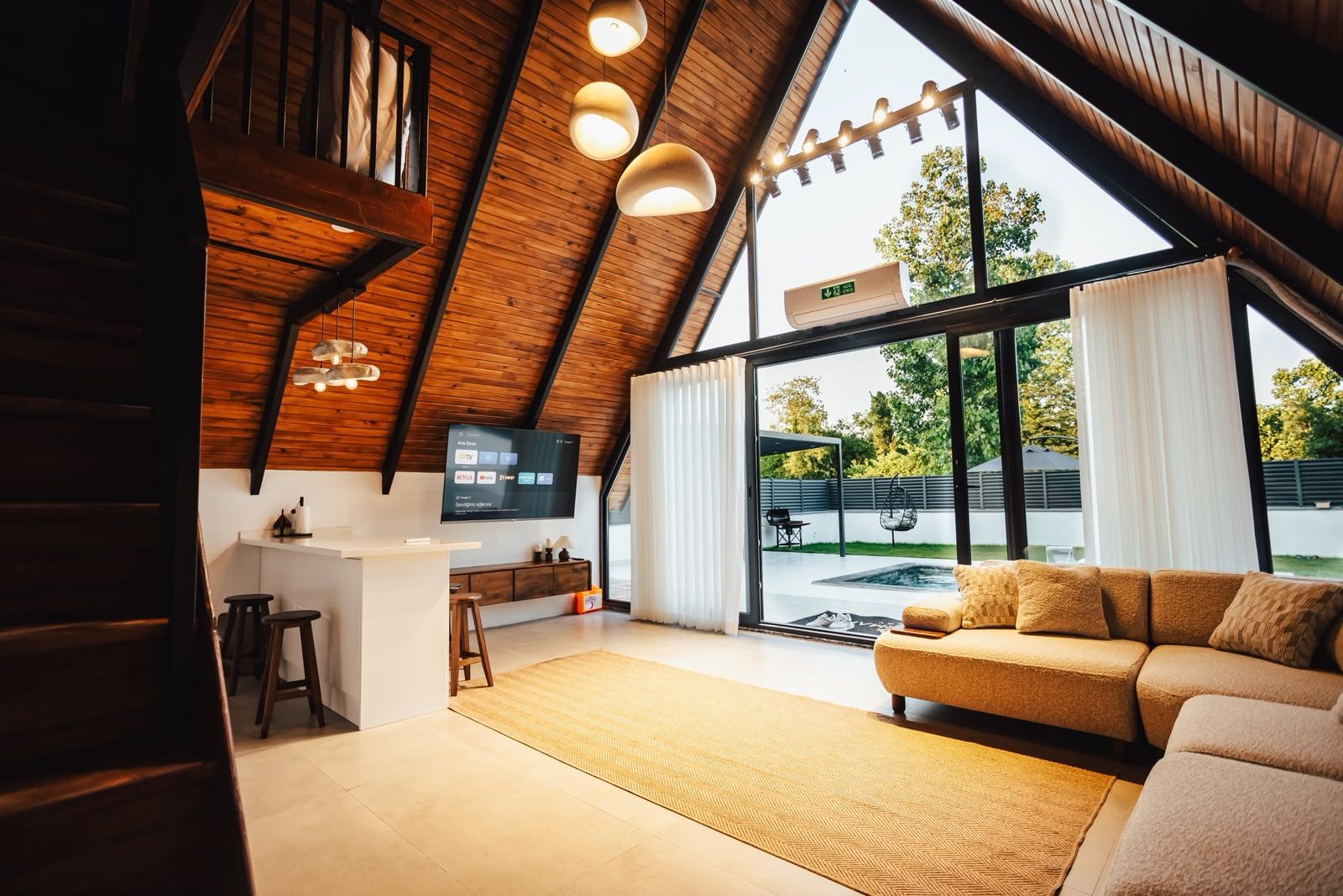 Een modern interieur met een schuine plafond, een flatscreen televisie aan de wand, een bank en een groot raam met uitzicht op het landschap.
