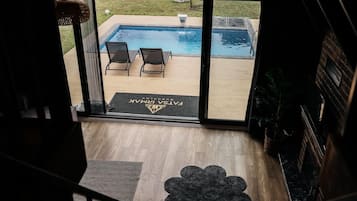 A view of a swimming pool with two lounge chairs, a doormat with a logo, and a wooden deck.