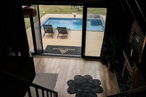 Vista de uma piscina com duas espreguiçadeiras, um tapete de entrada com logotipo e um deck de madeira.