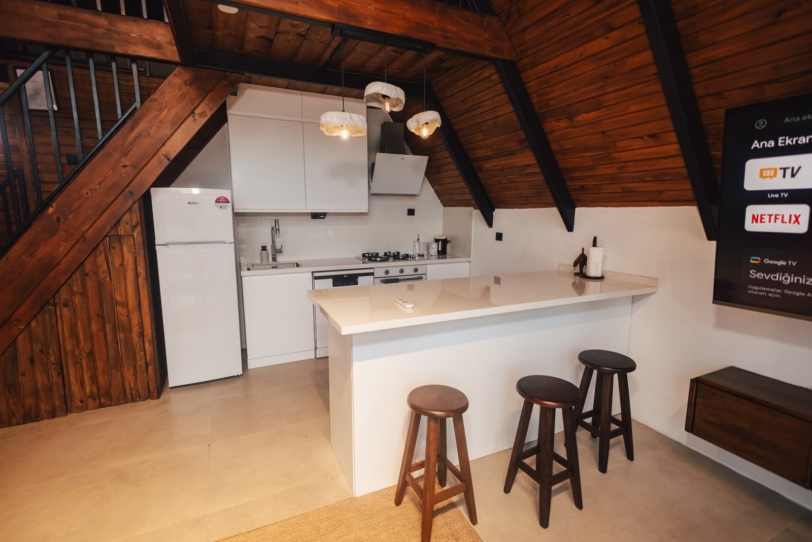 Une cuisine moderne dotée d’un îlot central, de touches de bois et d’un téléviseur fixé au mur qui permet d’accéder aux services de diffusion en continu.