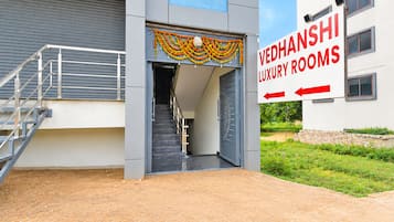 Una entrada de edificio con una escalera que lleva a una puerta, un letrero que indica 'VEDHANSHI LUXURY ROOMS' y un camino de acceso con portones.