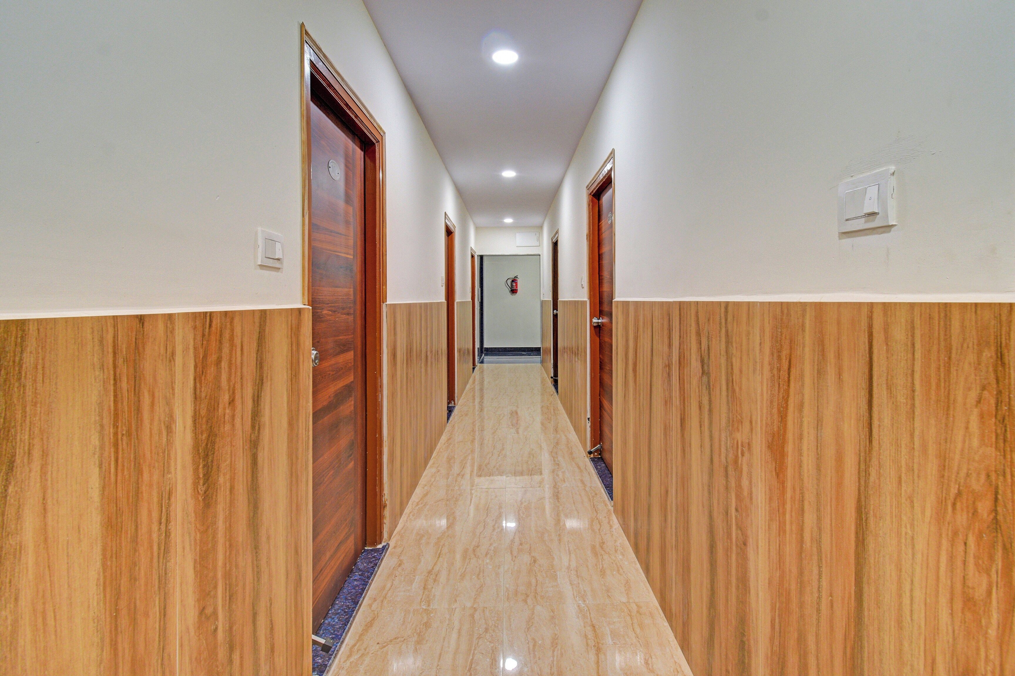 Un pasillo de hotel con paneles de madera y suelo de mármol, que conduce a una puerta al final.