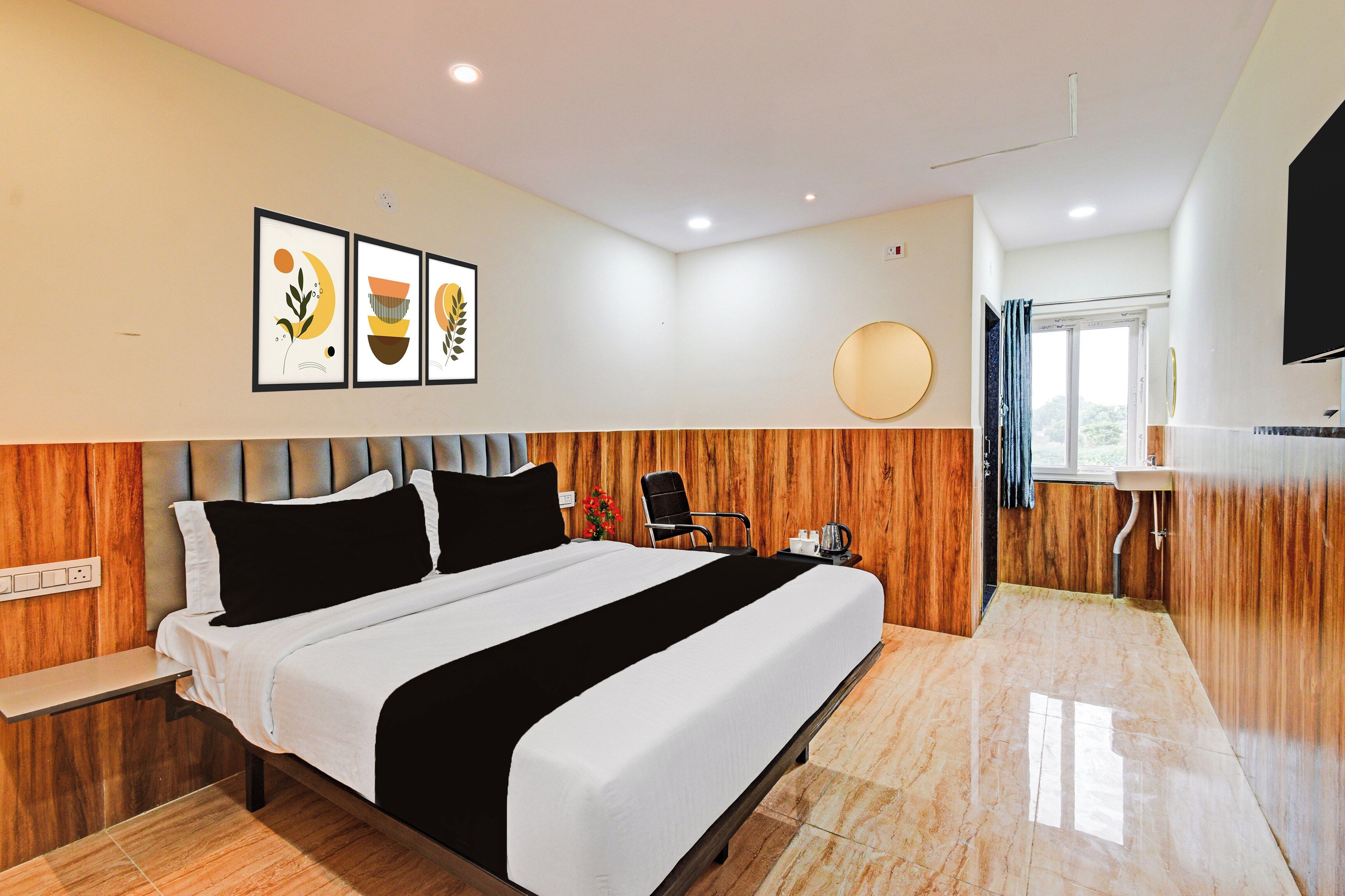 Habitación de hotel con cama, mesita de noche, una silla, una pequeña mesa con hervidor y televisor montado en la pared.