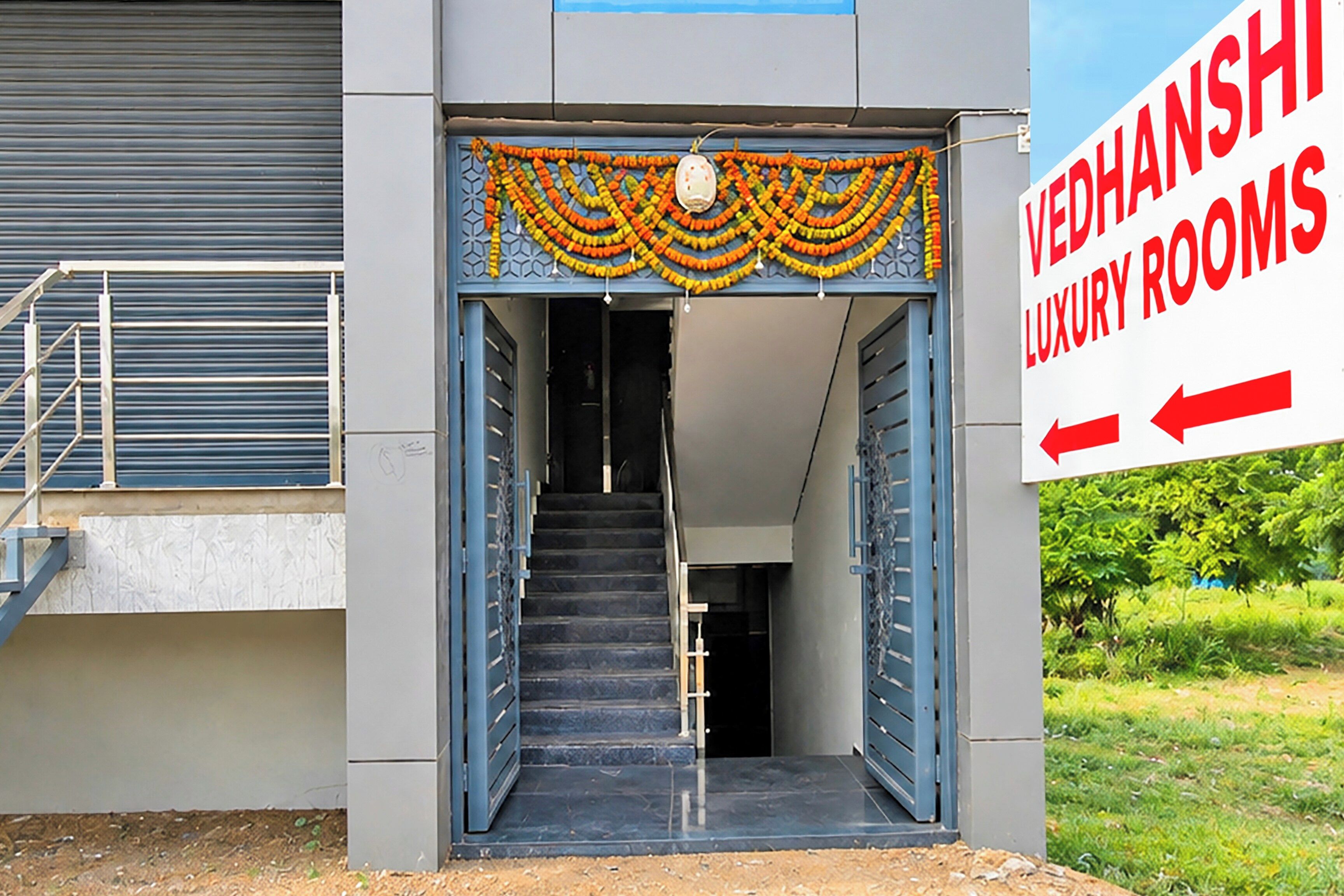 Entrada de un edificio con un letrero que dice 'Vedhanshi Luxury Rooms' y una escalera que conduce al interior.