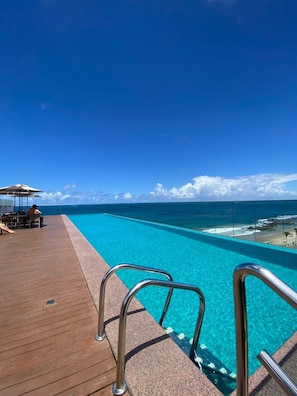 Ein Pool mit klarem, blauem Wasser, eine Holzterrasse und Meerblick.