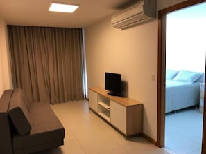 A modern living room with a sofa, a TV on a wooden stand, and an air conditioning unit on the wall. - New Listing (Salvador)