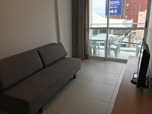 Ein modernes Hotelzimmer mit grauem Sofa, einem Flachbildfernseher und einem großen Fenster mit Blick nach draußen.
