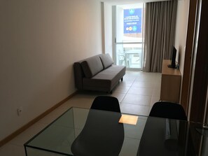 Ein Zimmer mit einem Glastisch, zwei Stühlen, einem Sofa und einem Fernseher.