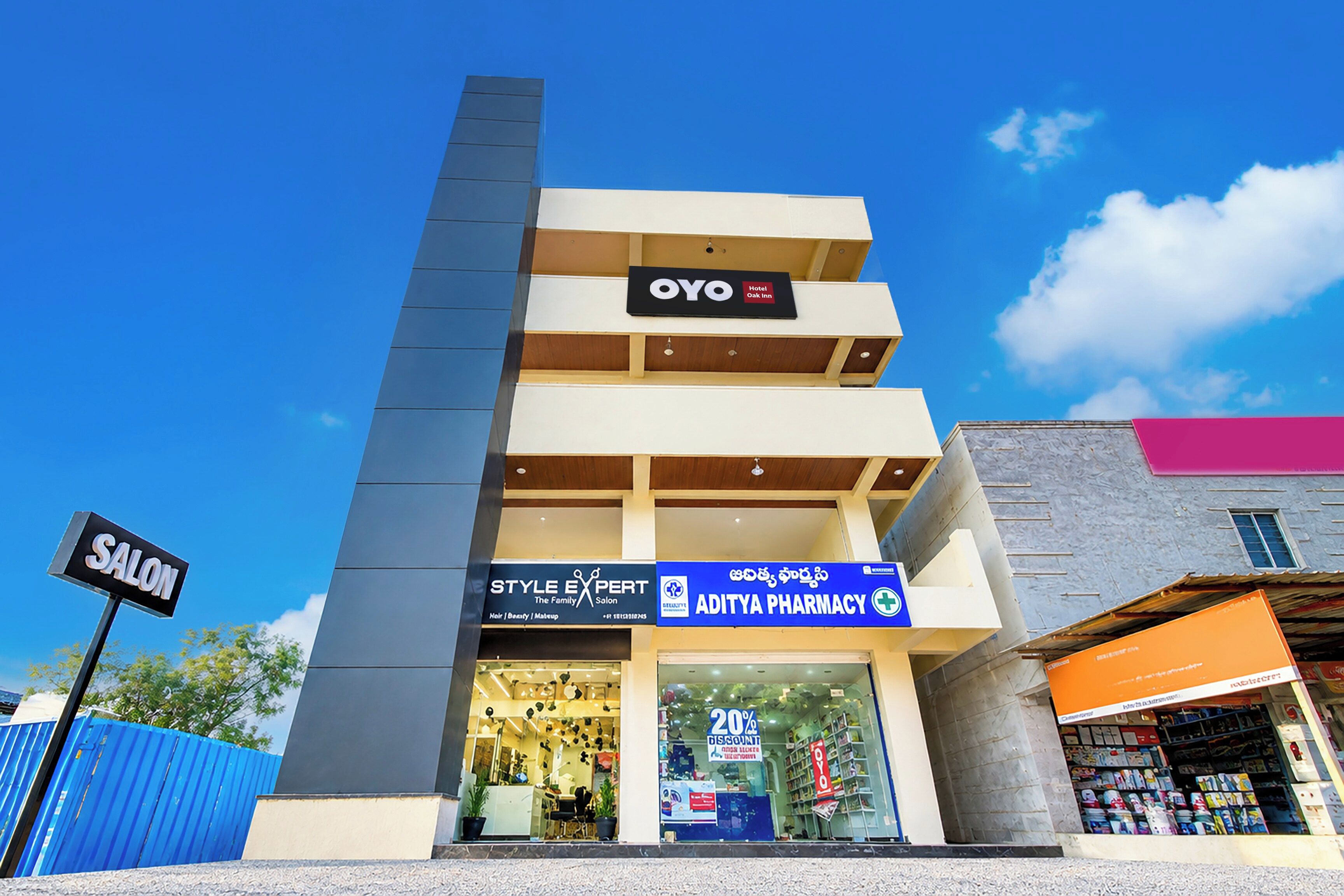 Un edificio de varios pisos con un llamativo letrero de OYO Hotel, un salón y una farmacia Aditya.