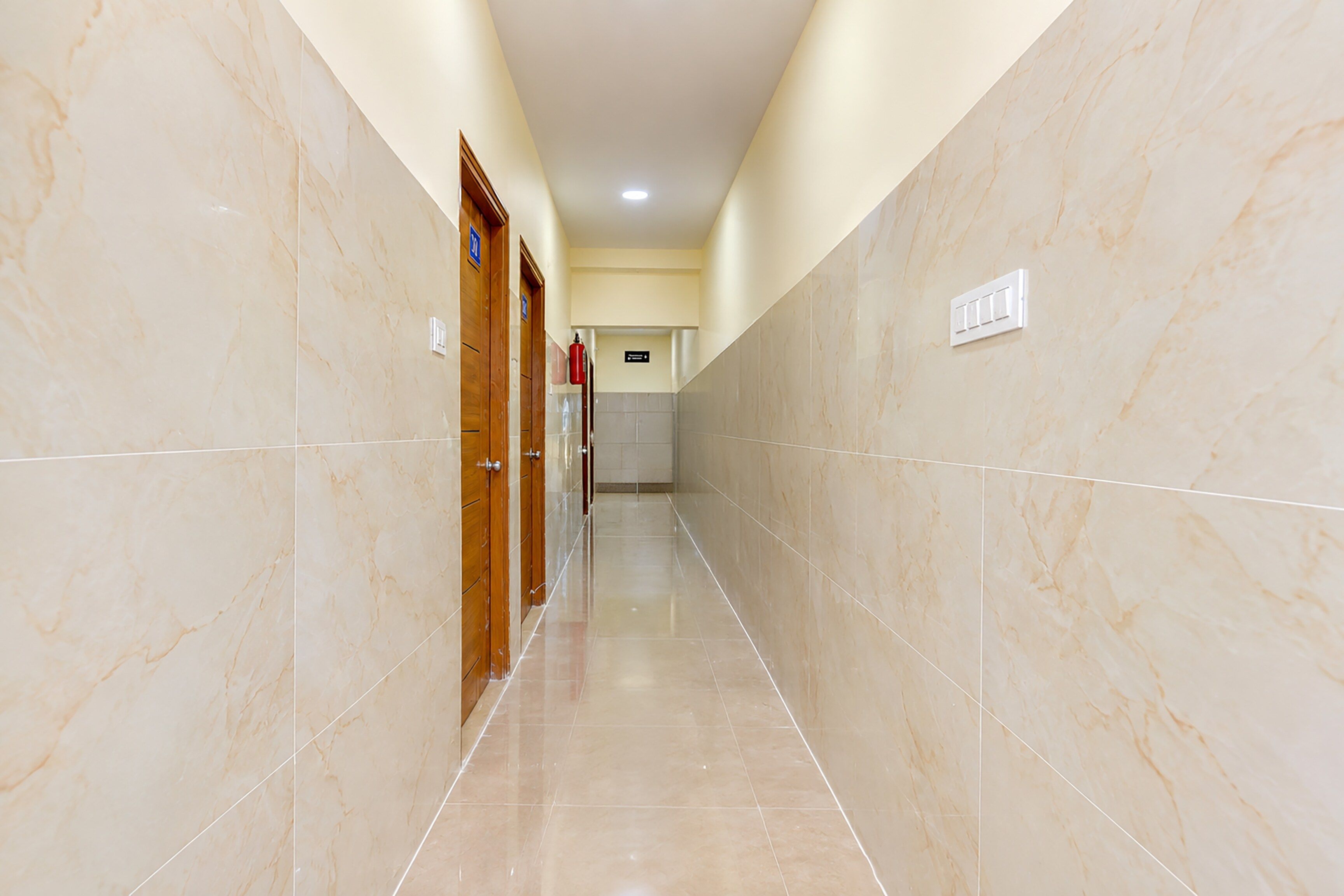 Un pasillo con paredes de mármol y puertas, que conduce a una habitación con piso de baldosas.