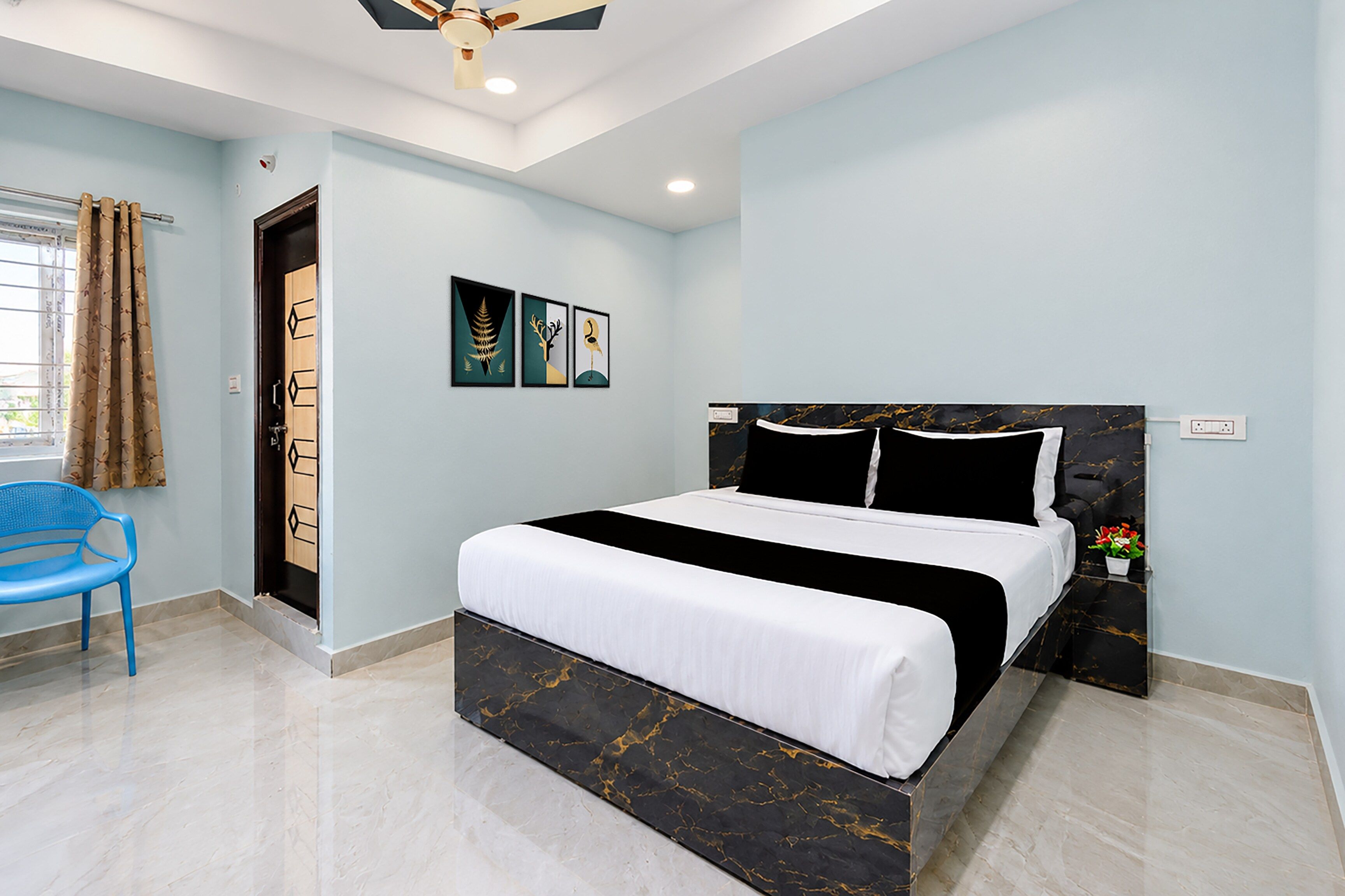 Un dormitorio con cama, una silla, ventilador de techo y obras de arte en la pared.