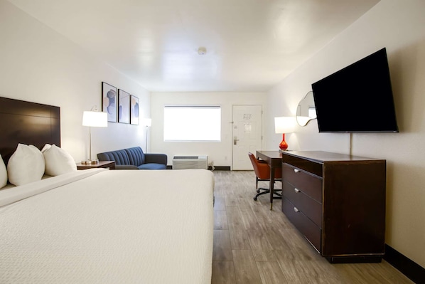 Une chambre d’hôtel équipée d’un lit, d’un bureau, d’une chaise, d’une télévision et décorée avec des œuvres d’art aux murs.