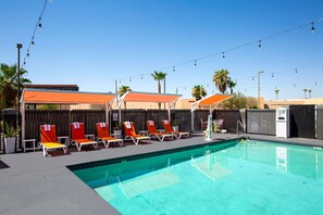 Une piscine entourée d’une clôture et de palmiers, avec des chaises longues et des parasols.