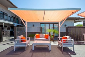 Une terrasse dotée de mobilier blanc, d’une table et d’un grand auvent.