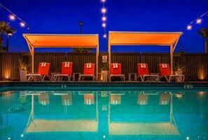 Piscina amb gandules sota una zona d'ombra, envoltada per una tanca i il·luminada per llums penjants.