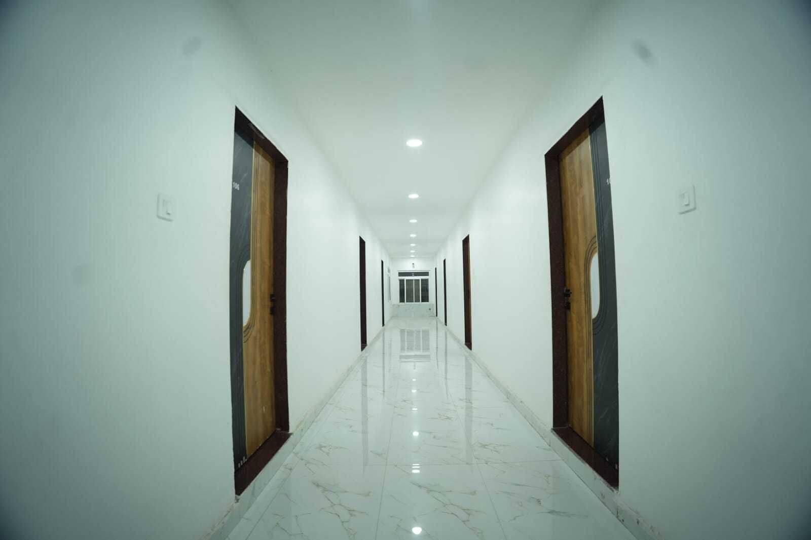 A long, straight hallway with white walls and a marble floor, leading to a door at the end.
