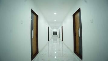 A long, straight hallway with white walls and a marble floor, leading to a door at the end.