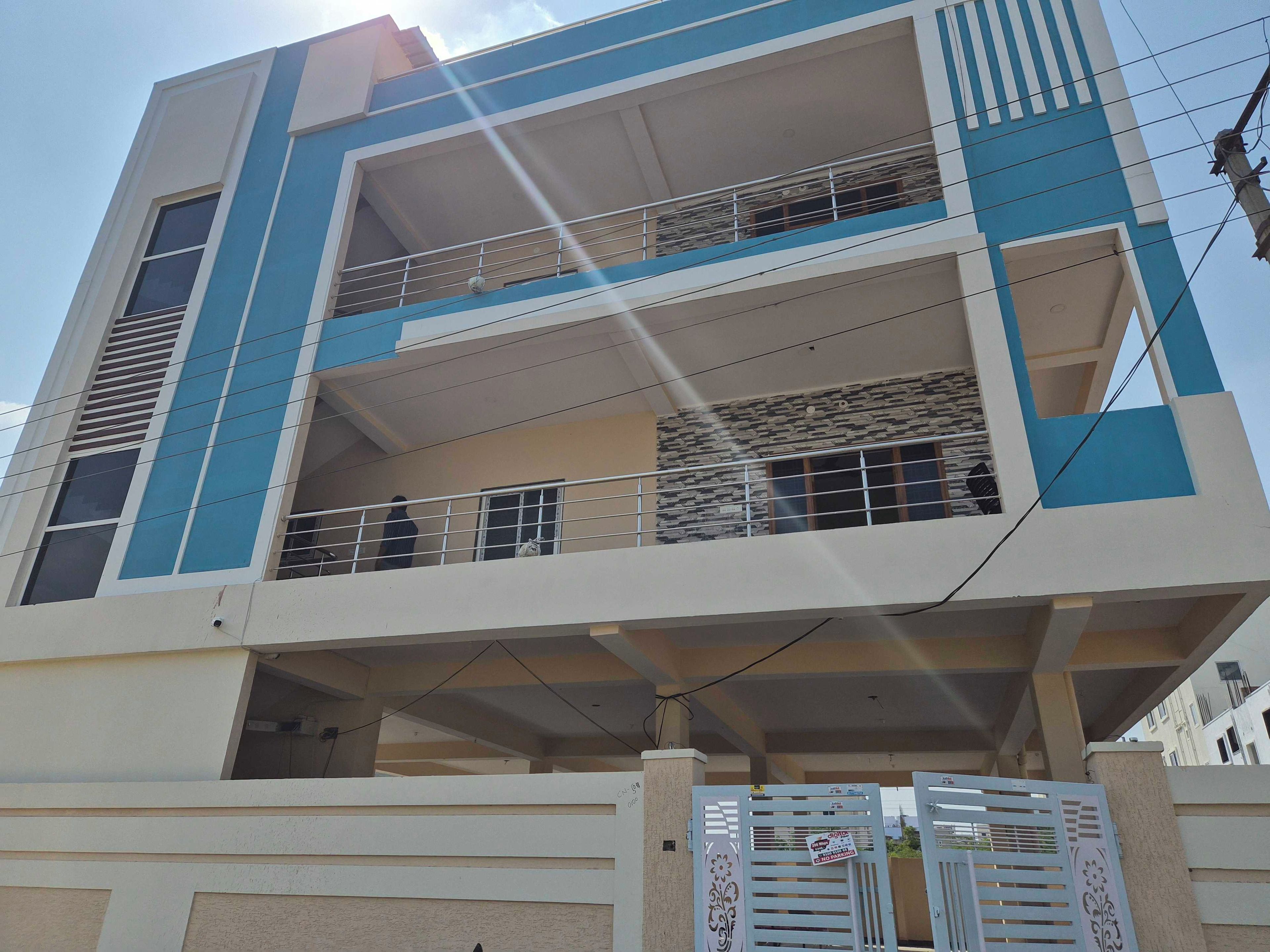 Un edifici residencial de diversos pisos amb balcons, una entrada tancada amb reixa i línies elèctriques visibles.