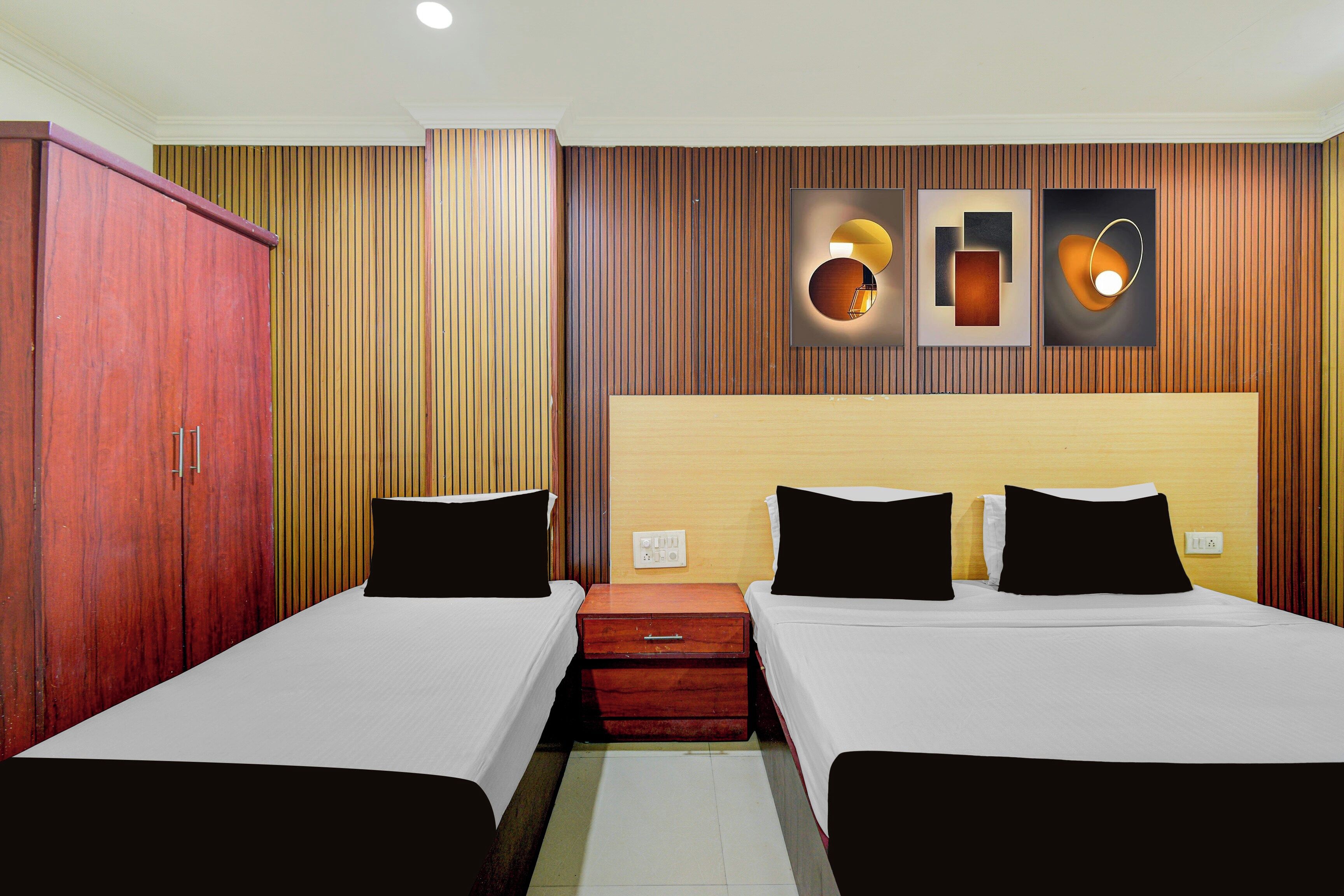 A hotel room with two single beds, a wooden wardrobe, and a wall-mounted light fixture.