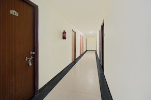 Un pasillo con puertas de madera, un extintor montado en la pared y un suelo de baldosas.