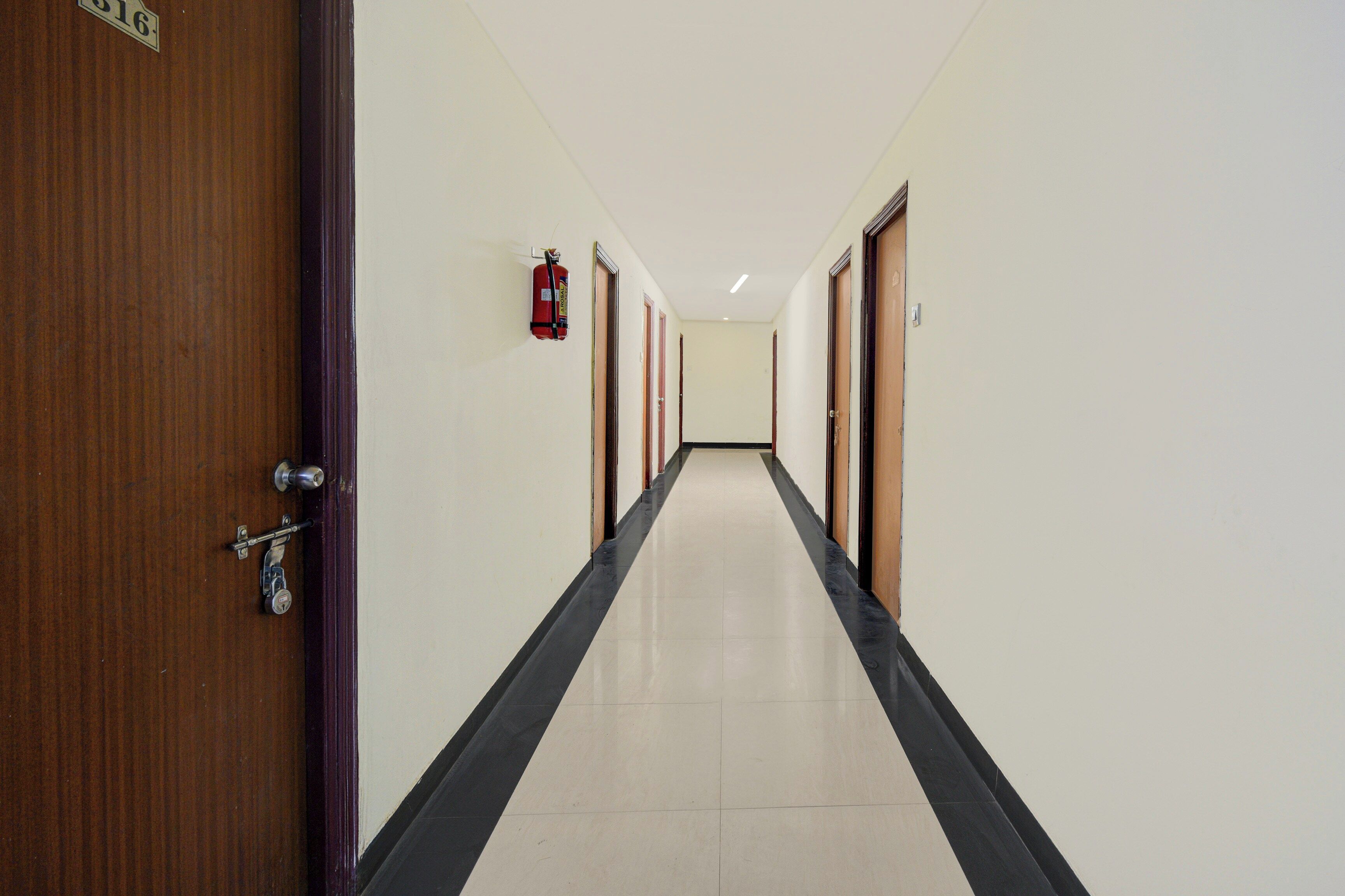 A corridor with doors on both sides, a fire extinguisher mounted on the wall, and a tiled floor.