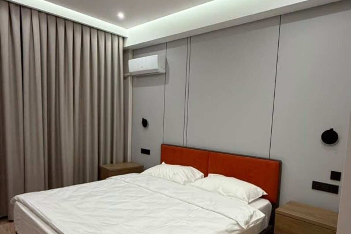 Una habitación de hotel moderna con una cama grande, suelo de madera e iluminación empotrada en el techo.