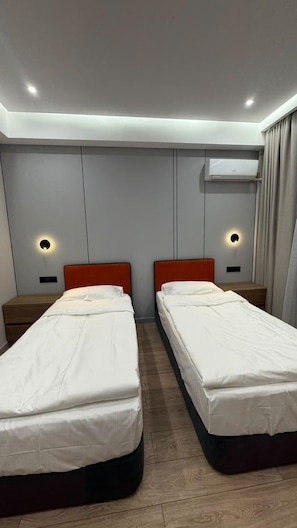 Ein Hotelzimmer mit zwei Betten, einer Wandklimaanlage und Nachttischlampen.