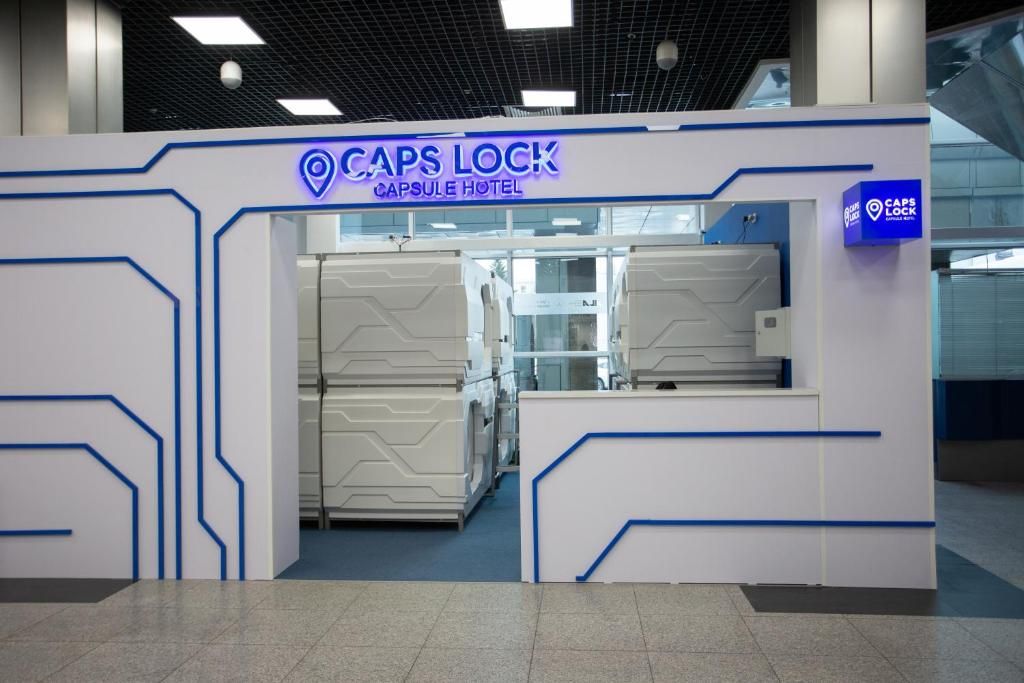 Entrada de un hotel cápsula con un diseño moderno, destacando un cartel con la leyenda 'Caps Lock Capsule Hotel'.
