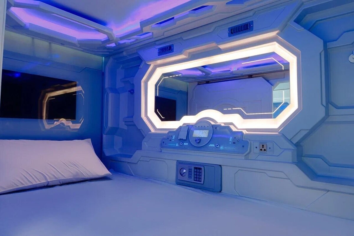 A futuristic room with a bed, a control panel, and a large window.