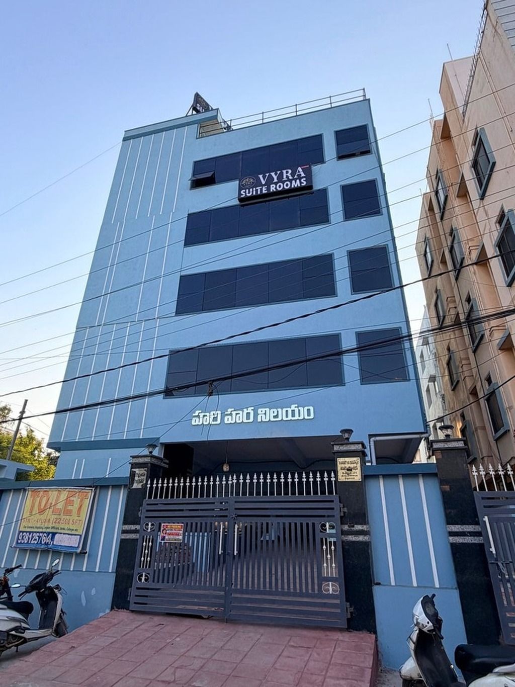 Um edifício com uma placa indicando 'VYRA SUITE ROOMS' e uma entrada gradeada.