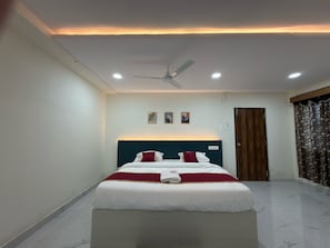 A hotel room with a bed, ceiling fan, recessed lighting, a door, and a window with curtains.