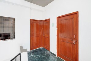Un pasillo con dos puertas de madera, una ventana con barrotes y un suelo de mármol.