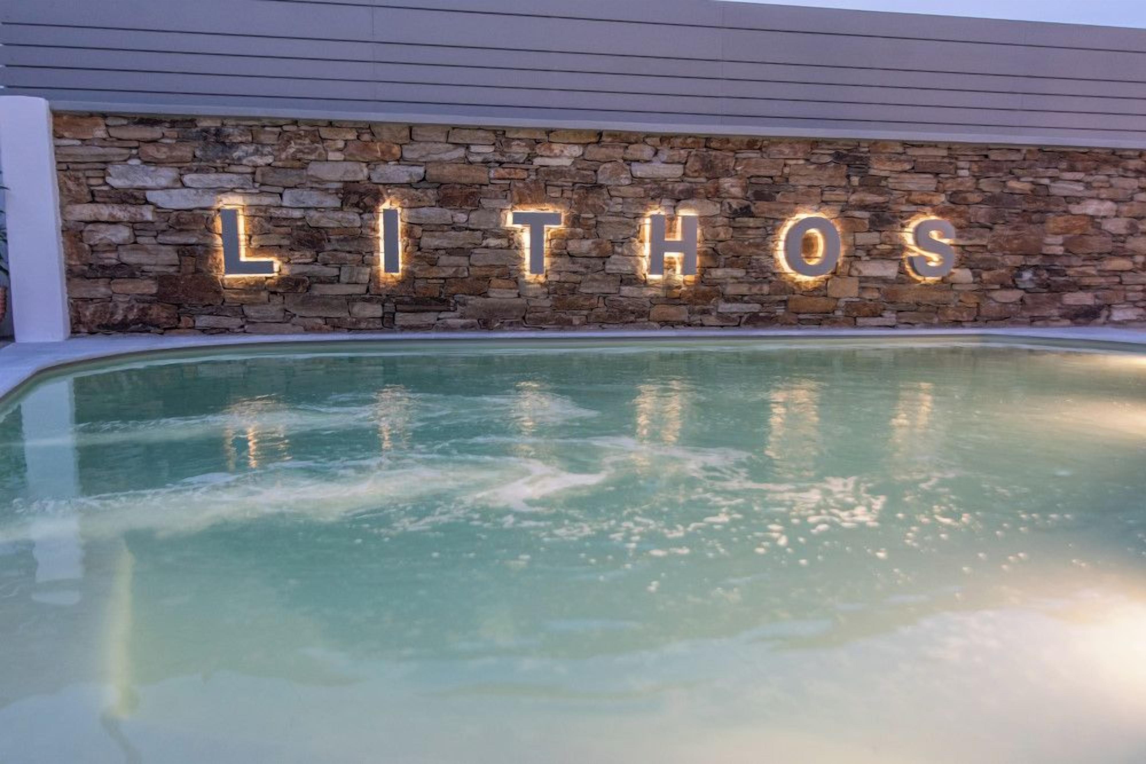 Un espace piscine agrémenté d’un mur en pierre et de lettres illuminées formant le mot « LITHOS ».