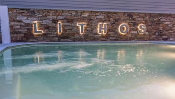 Un espace piscine agrémenté d’un mur en pierre et de lettres illuminées formant le mot « LITHOS ».