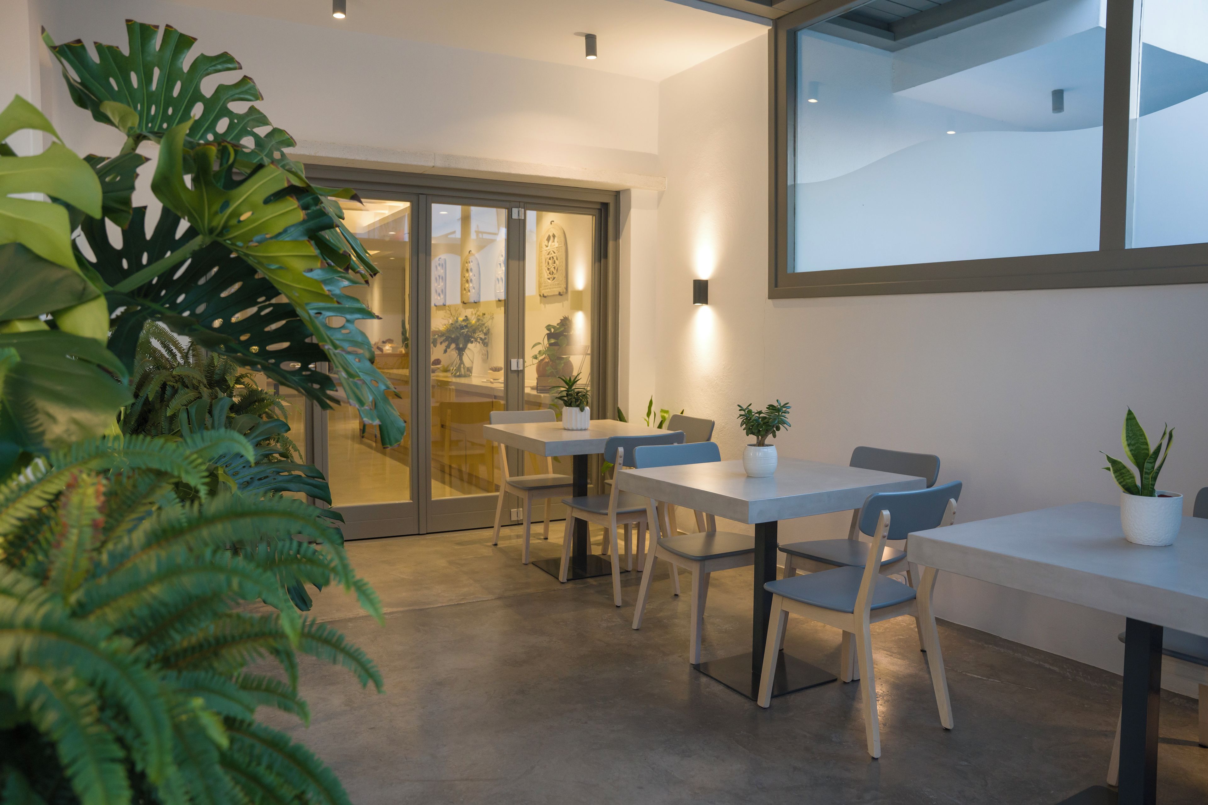 Un intérieur moderne avec une porte vitrée donnant sur un espace repas, comprenant des tables, des chaises et des plantes en pot.