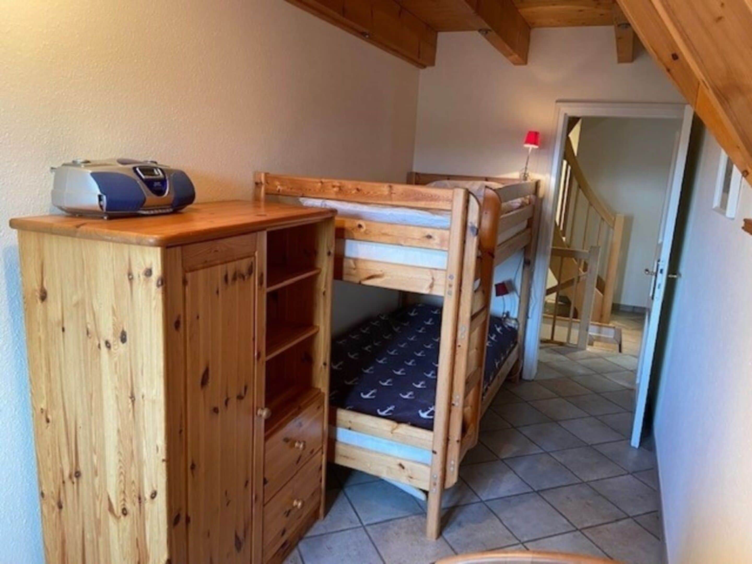 A small, compact room with a bunk bed, a wooden cabinet with drawers, and a red lamp.