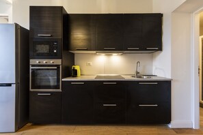 Une cuisine moderne avec des meubles de couleur sombre, un four encastré, un four à micro-ondes et un évier en acier inoxydable.