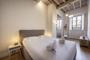A bedroom with a large bed, bedside lamp, and a wooden nightstand. - Colonna Suite by MMega Homes and Villas (Florence)