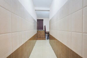 A corridor with tiled walls and a tiled floor, leading to a staircase with a door at the end. - Hotel O Rock Beachview Pondicherry (Puducherry)