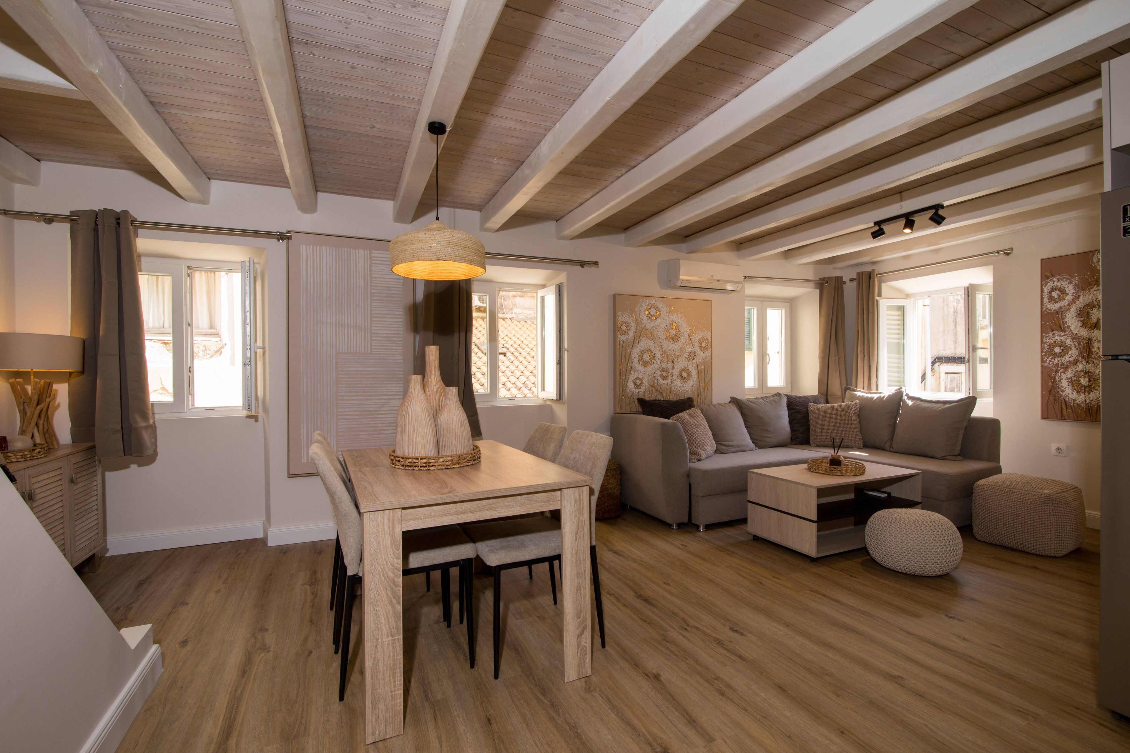 A modern living room with a wooden dining table, a sofa set, and a hanging light fixture.