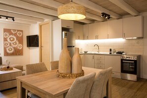 A modern kitchen with white cabinets, a stainless steel oven, and a dining area with a wooden table and chairs. - Alto Residences by CorfuEscapes  (Corfu)