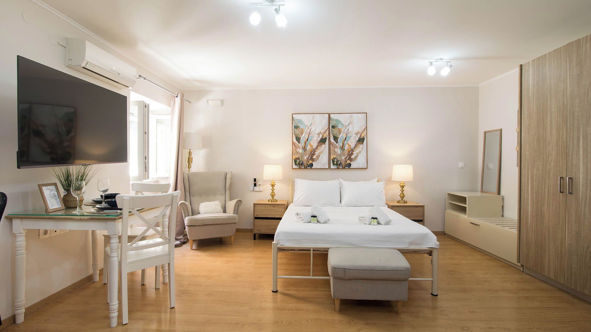 A hotel room with a bed, bedside tables, a desk, a chair, a TV, artwork on the wall, and a wardrobe.