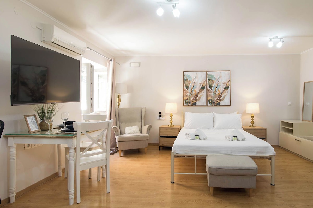 A hotel room with a bed, bedside tables, a desk, a chair, a TV, artwork on the wall, and a wardrobe.