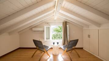 Amplia habitación en el ático con techo inclinado, dos sillas, una mesita y una ventana con vistas a la vegetación.