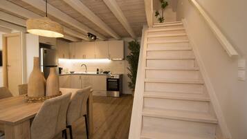 Une cuisine moderne avec des meubles blancs, un coin repas doté d’une table et de chaises en bois, et un escalier menant à l’étage supérieur.