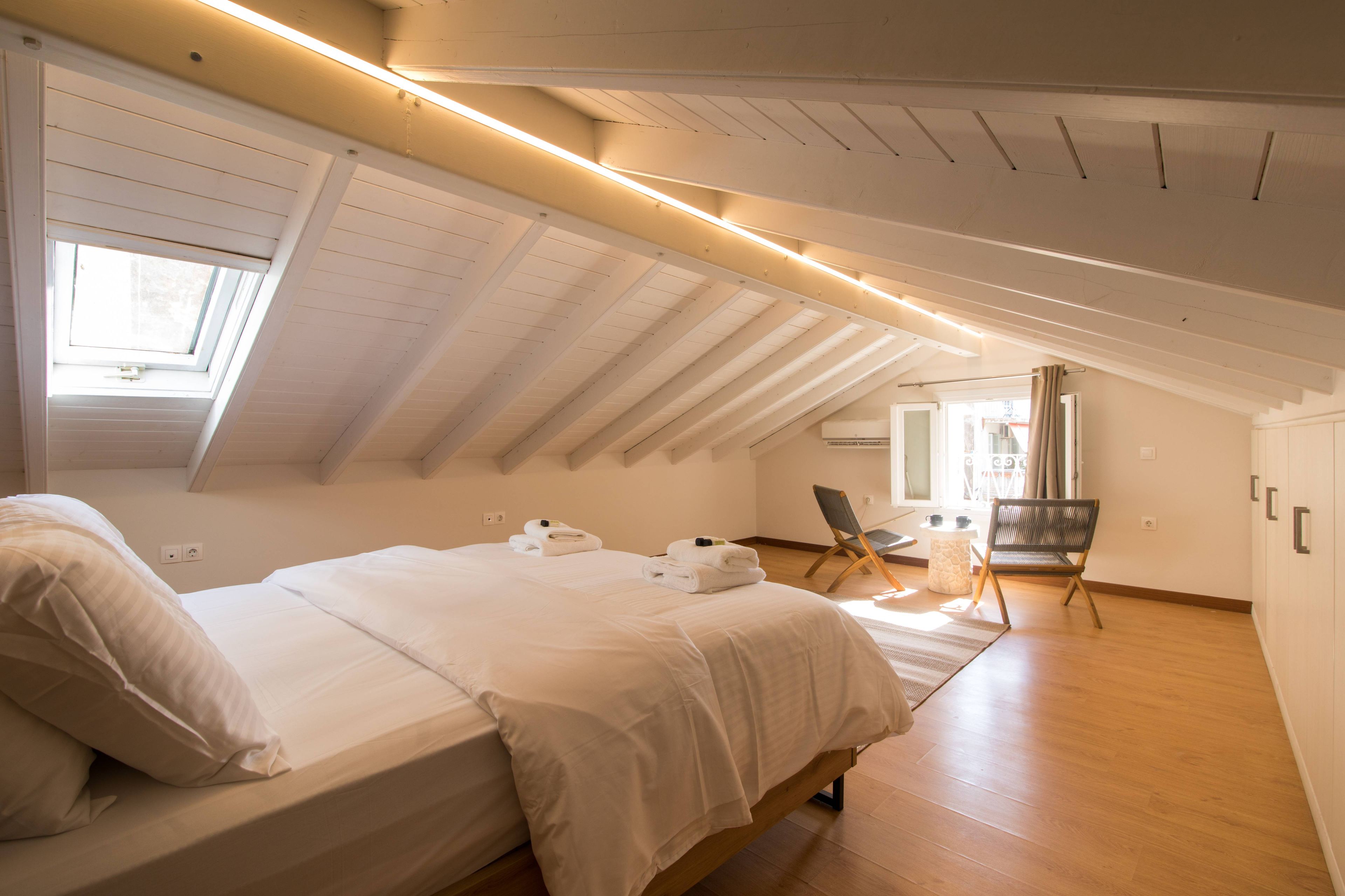 Une chambre avec un plafond en pente, un lit avec du linge de lit blanc, une chaise et une petite table.