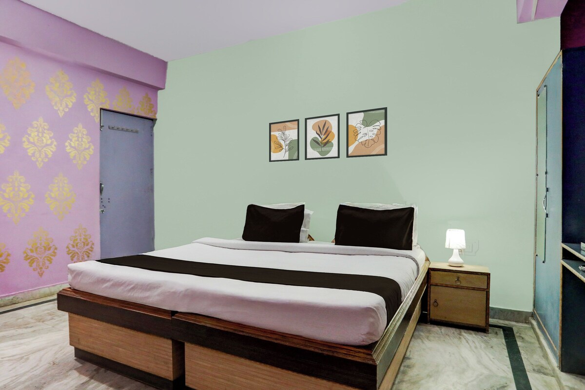 Un dormitorio con cama, almohadas, una mesita de noche, lámpara y decoración en la pared.