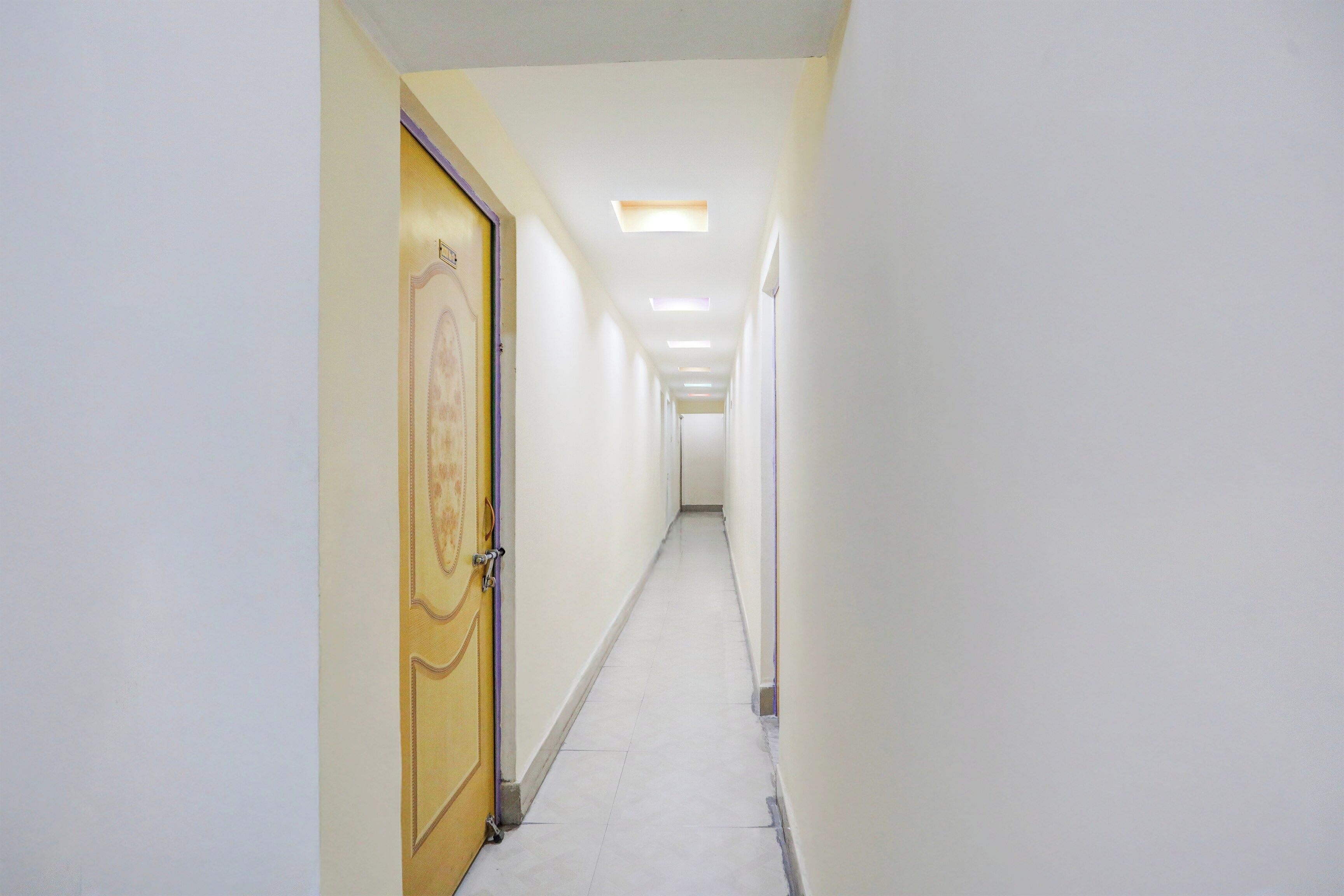 Un pasillo estrecho y bien iluminado, con una puerta de madera a la izquierda y una pared blanca a la derecha.
