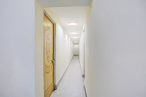 A narrow, well-lit hallway with a wooden door on the left and a white wall on the right. - Super Hotel O Anjanpeer Post Office (Hajipur)